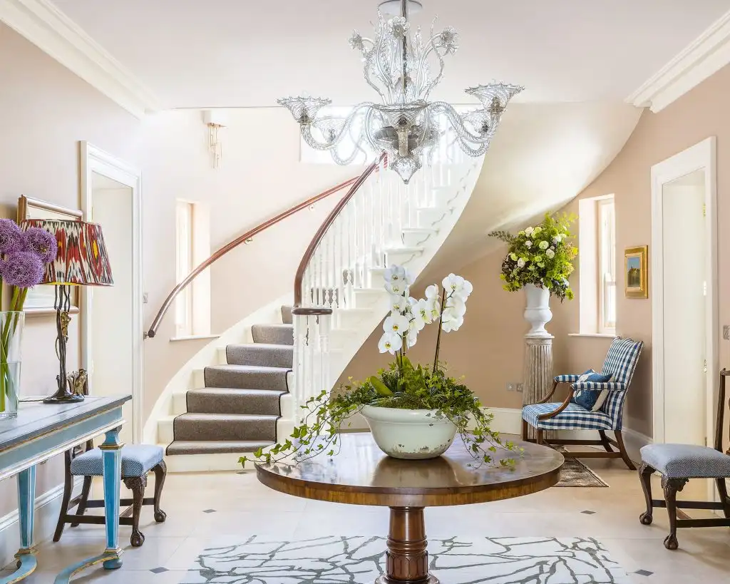 Bright traditional entry hall with a curved staircase, crystal chandelier, and pastel furnishings